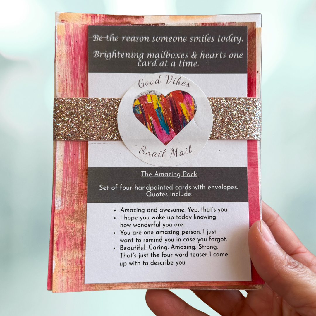 Good Vibes Snail Mail “The Amazing Pack” featuring four handpainted encouragement cards with uplifting quotes, wrapped with a glitter band and heart sticker, designed to brighten mailboxes and send meaningful handwritten connection.