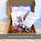 Unboxing view of the Good Vibes Snail Mail creative art kit with handmade cards, paints, brushes, wax seals, and supplies ready for thoughtful gifting